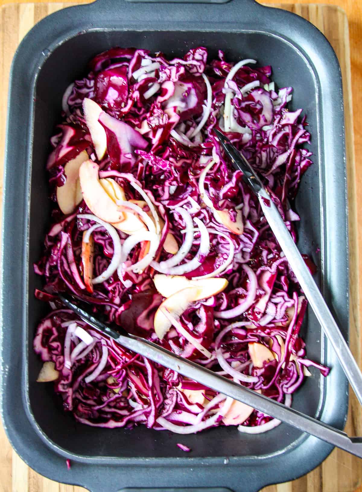 The ingredients being tossed together in the slow cooker with tongs.