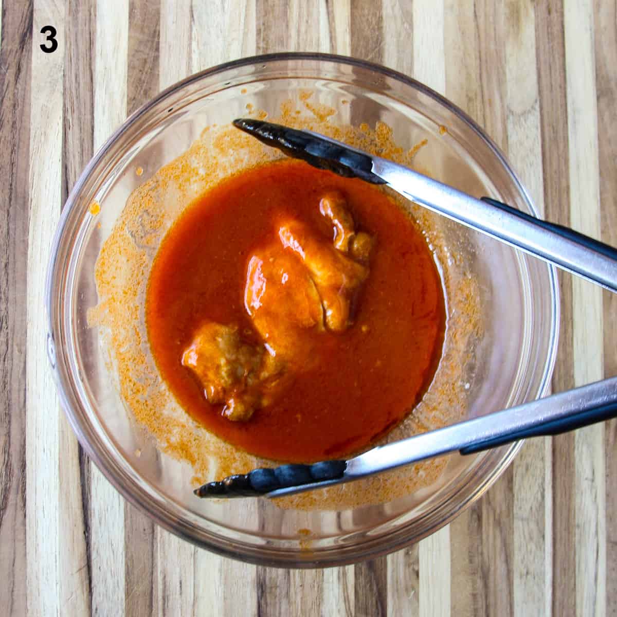 The third step in making the recipe; coating the chicken with buffalo sauce.