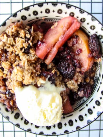 Apple and blackberry crumble in a dish on a wire rack.