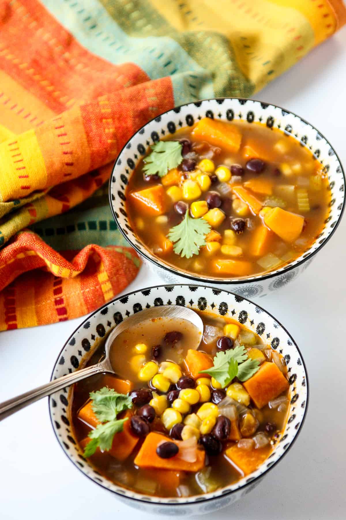Two bowls of sweet potato and black bean soup next to a brightly colored napkin.