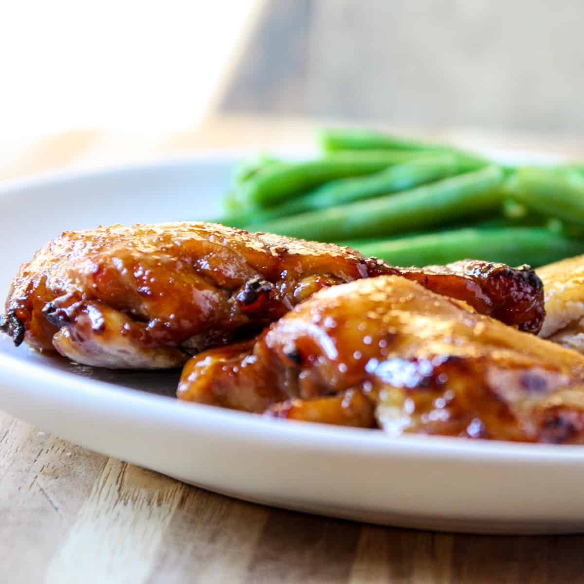 A side view of the chicken on a plate with green beans blurred in the background.