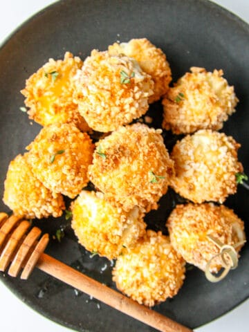 Several fried goat cheese balls on a black plate.