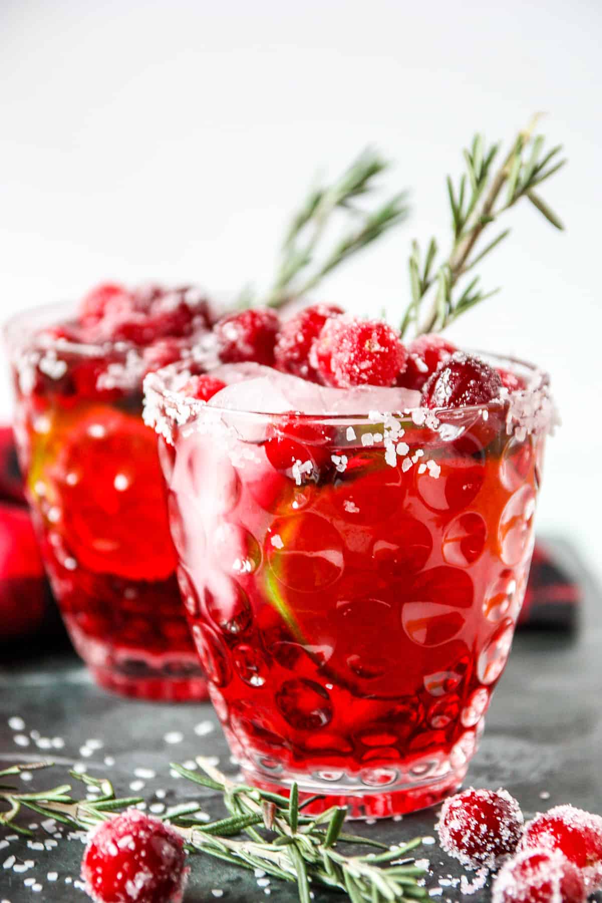 Two glasses mistletoe margarita topped with sugared cranberries.