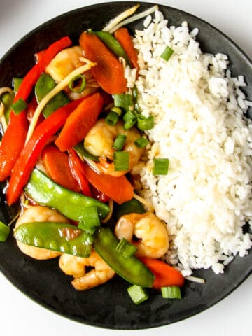 Shrimp chop suey and rice on a black plate.