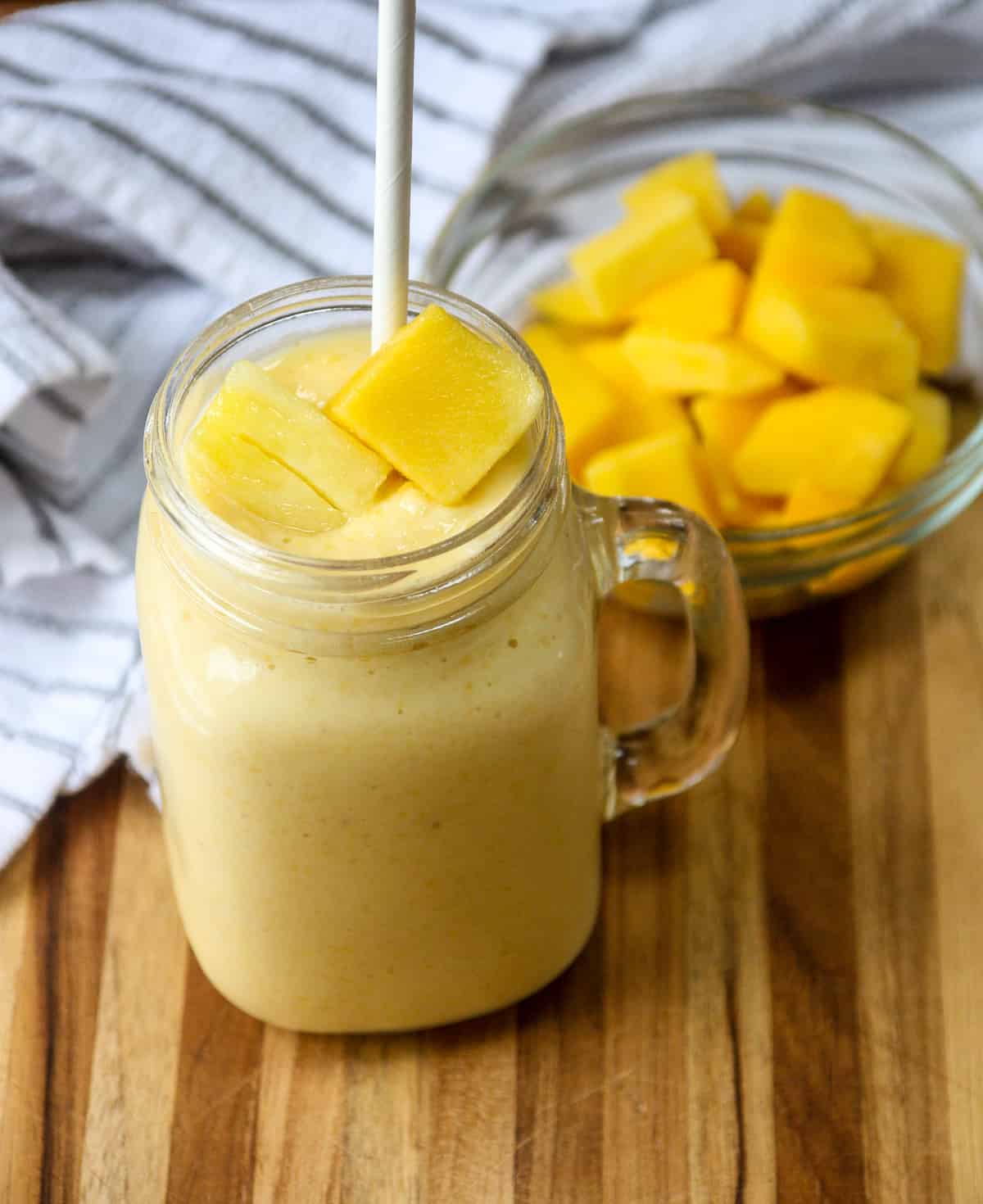 Mango Pineapple Smoothie in a glass mug with a white paper straw.