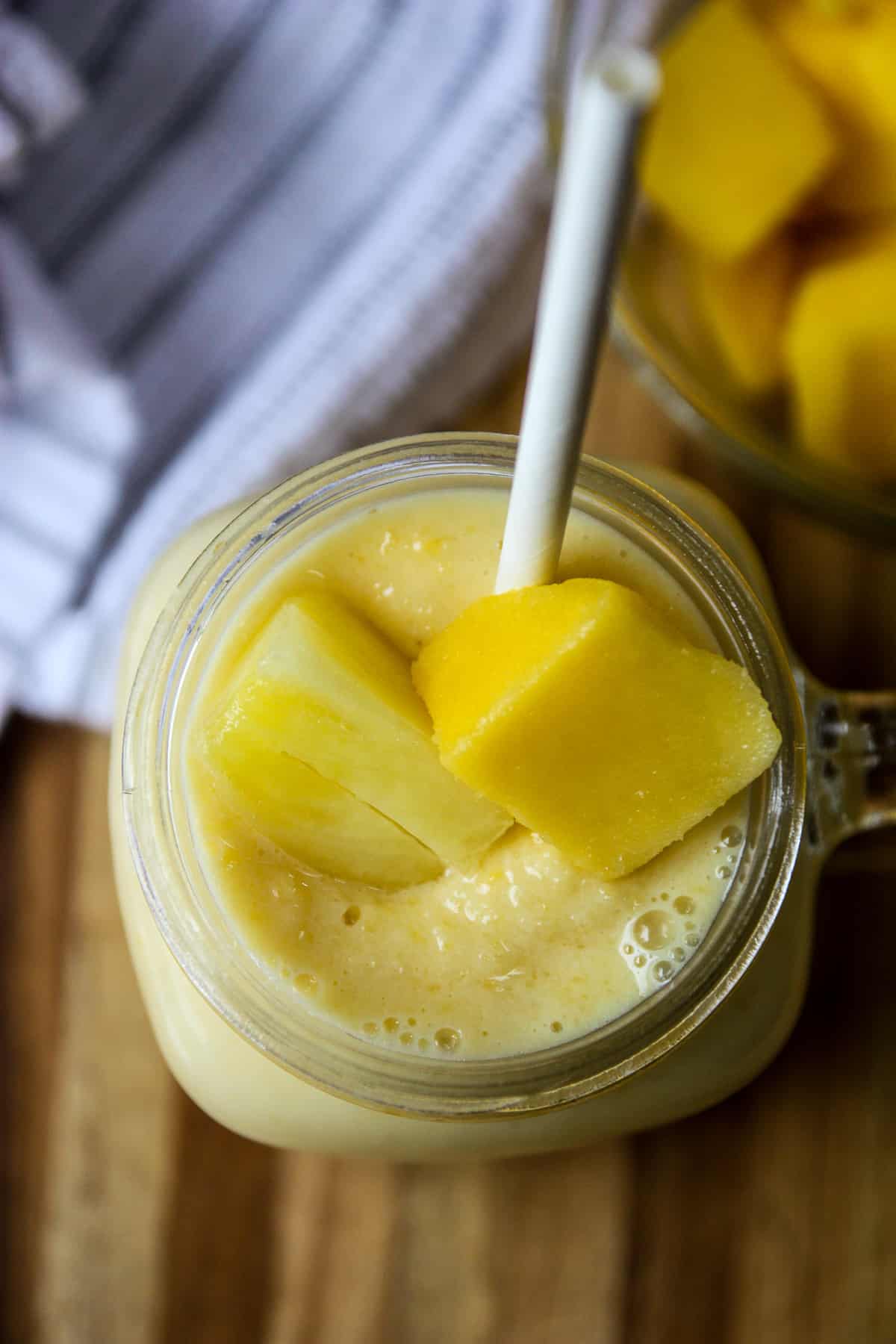Chunks of mango floating on top of a smoothie in a glass.