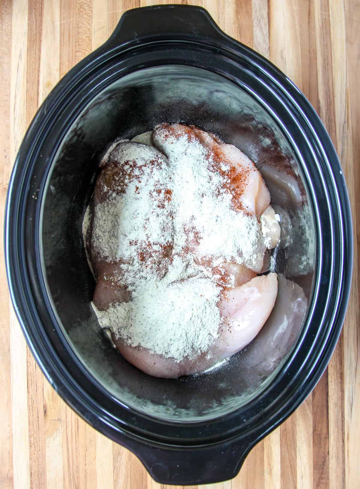 The chicken and seasonings in the bottom of the slow cooker.