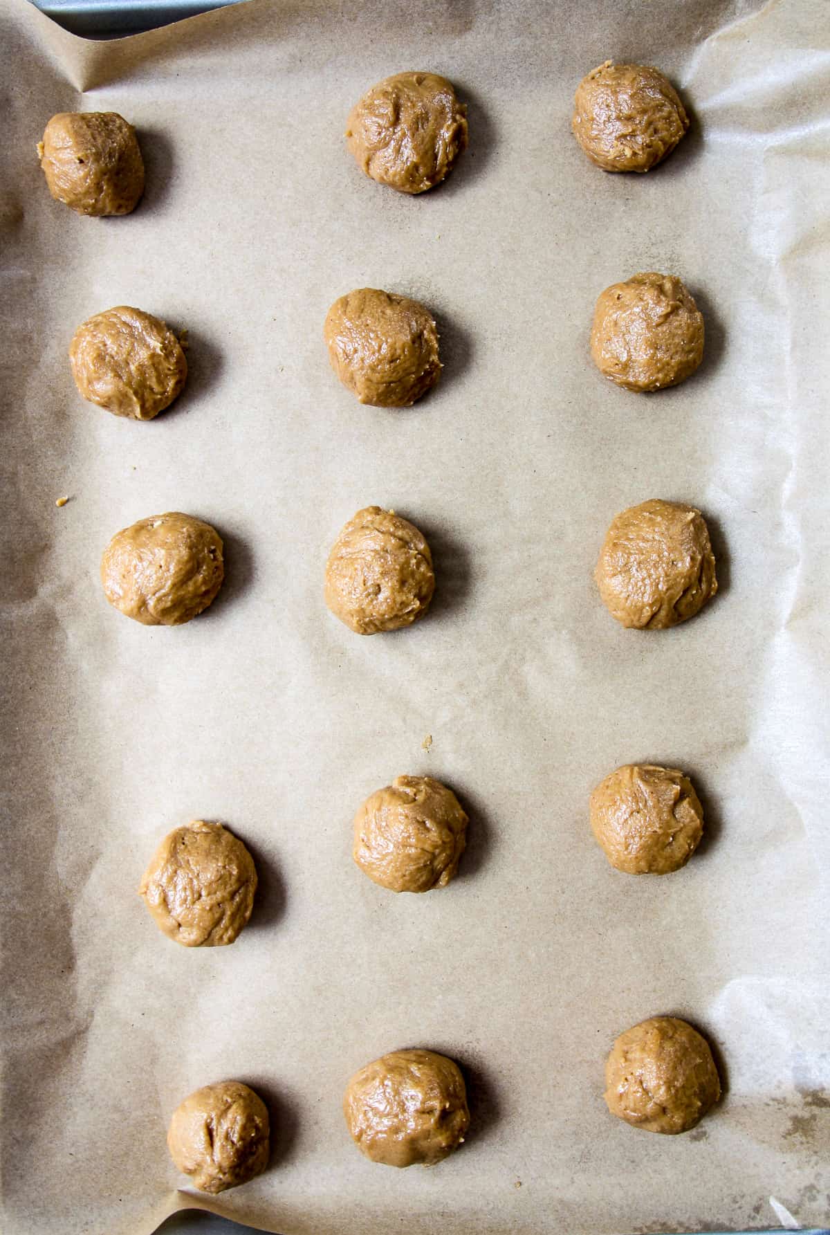 Cookie dough balls on a parchment lined baking sheet.