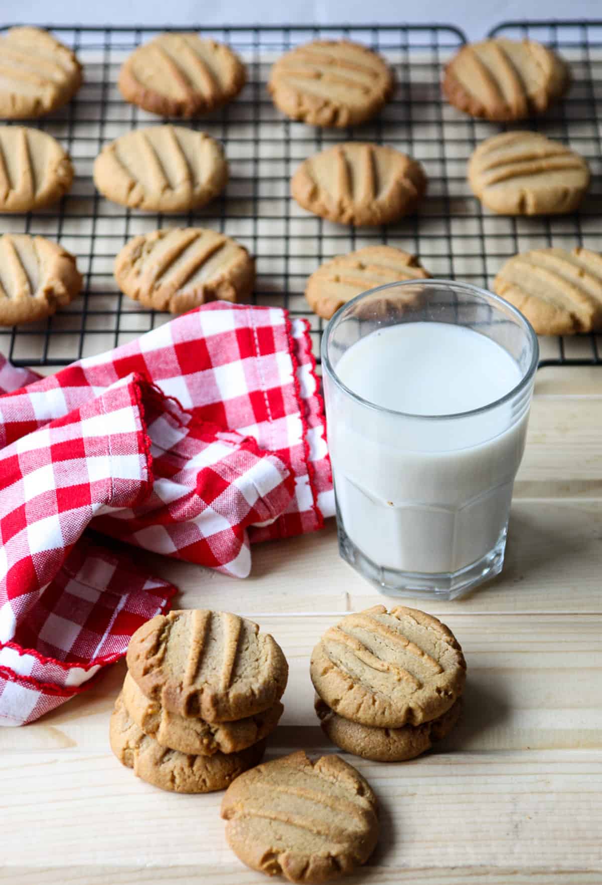 Gluten free peanut butter cookies and a glass of milk, in front of a wire rack with cookies cooling.