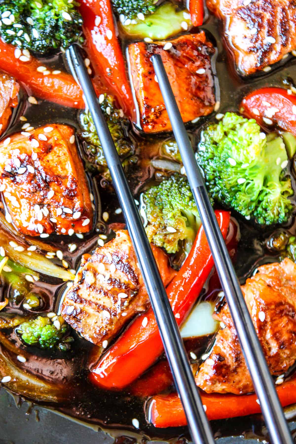 Salmon and vegetables in teriyaki sauce  with black chopsticks.