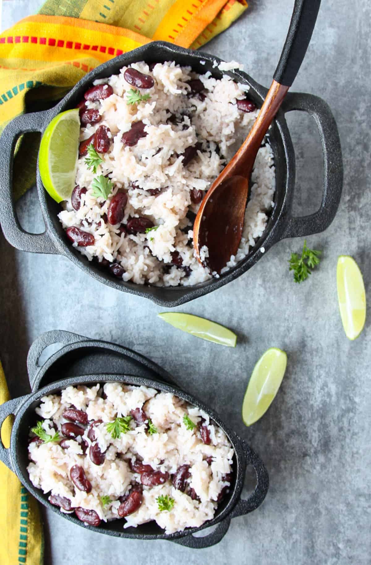 A pot of rice and beans being served onto cast iron plates with a wooden spoon.