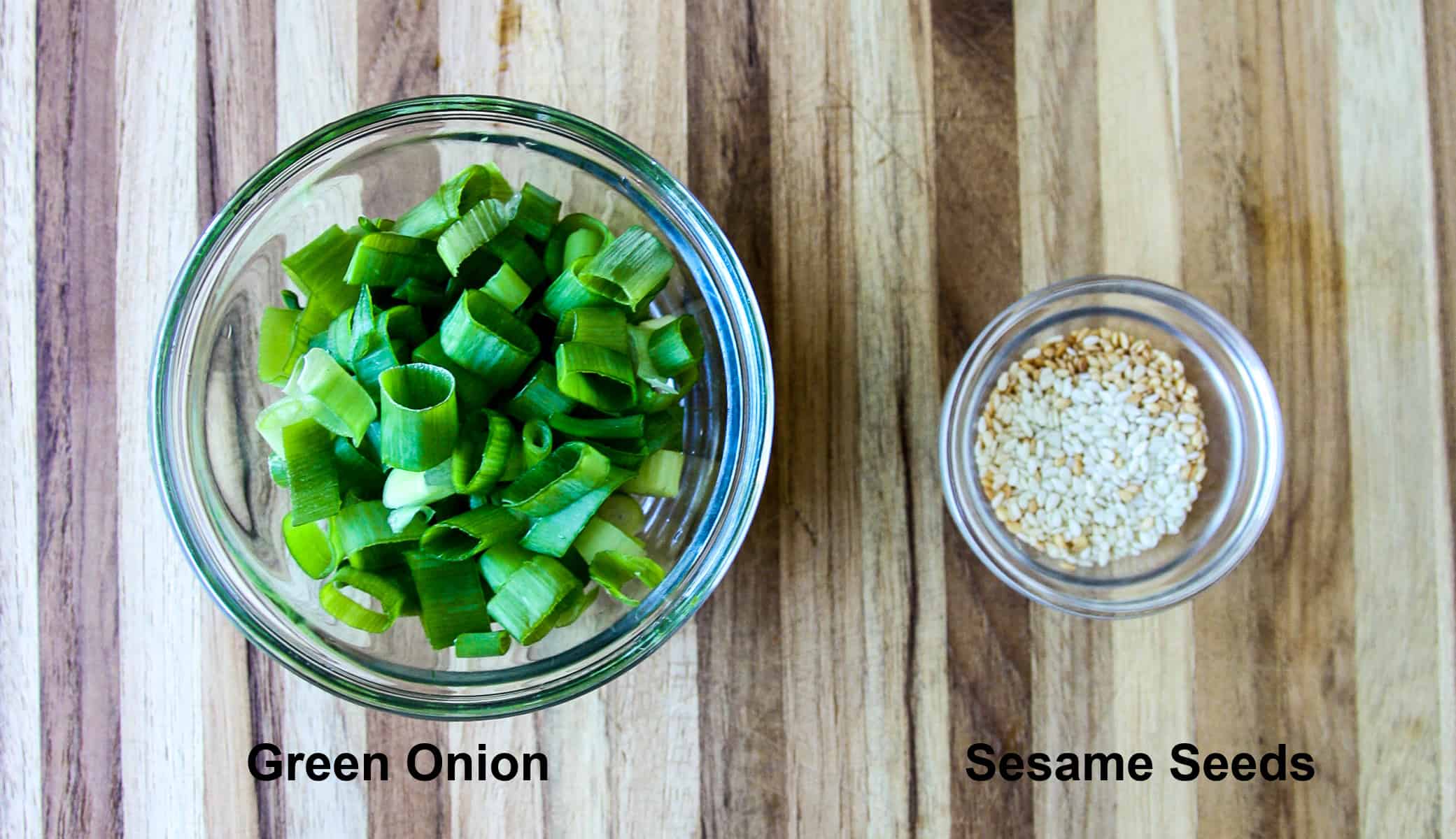 The meatball garnish ingredients, sliced green onion and sesame seeds, in glass bowls.