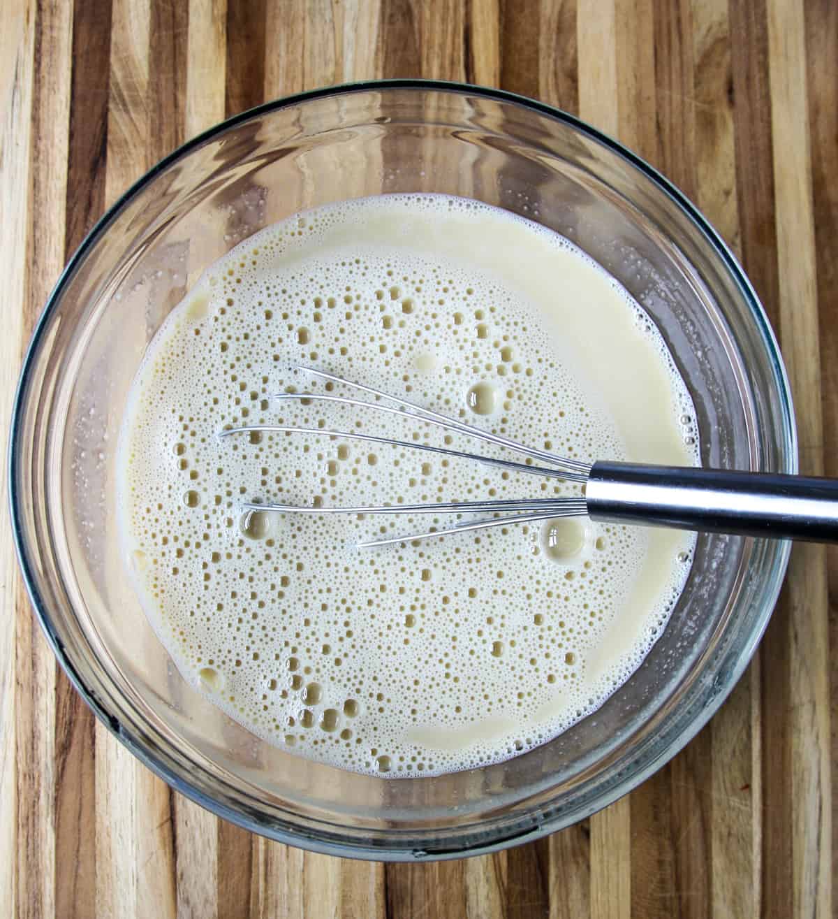 Custard ingredients being whisked together in a glass bowl.