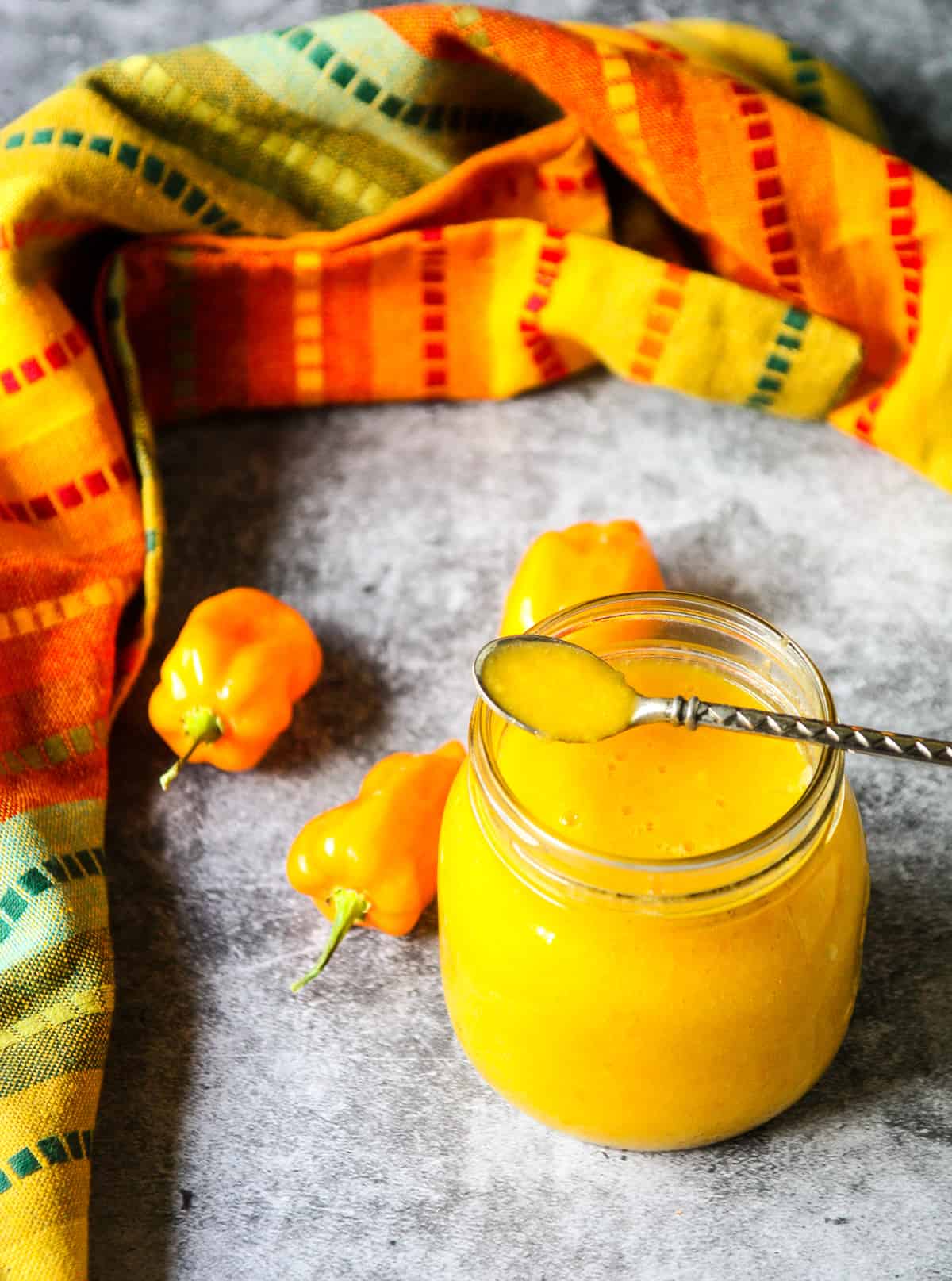 A small spoon dipping into a glass jar of mango habanero hot sauce.