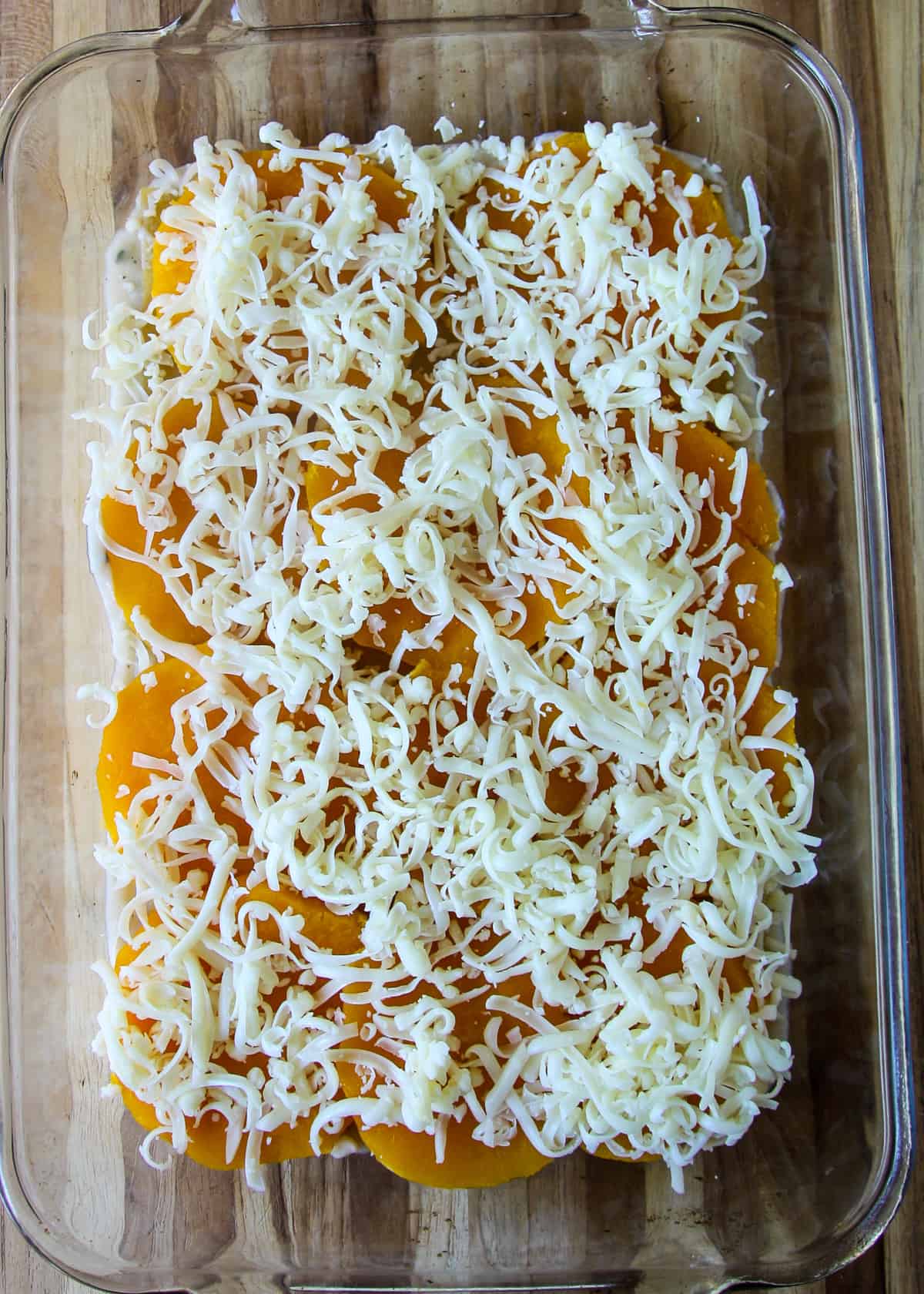 Shredded mozzarella cheese scattered over squash slices in the lasagna pan. 