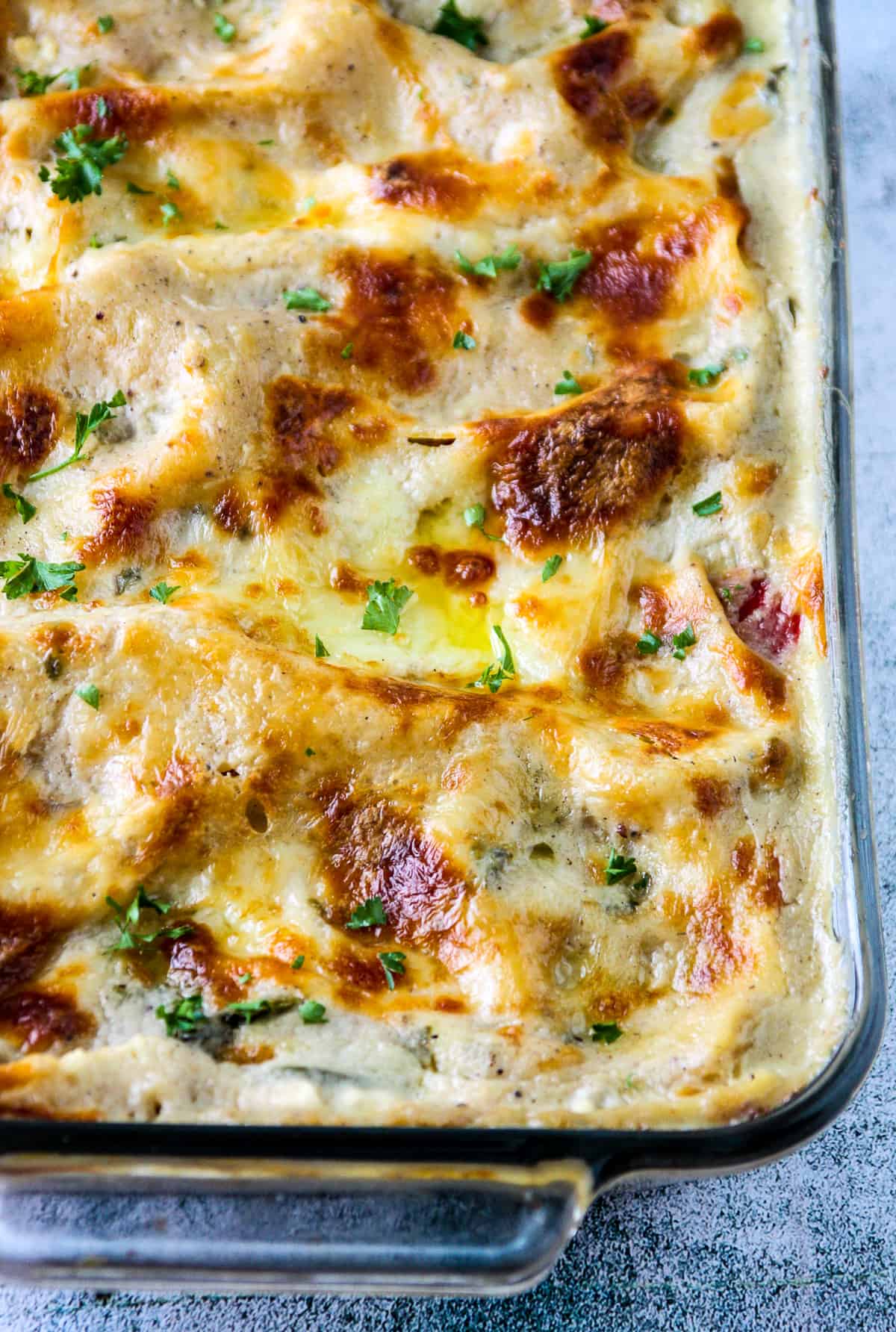 A baked vegetable lasagna with white sauce in a glass baking dish.