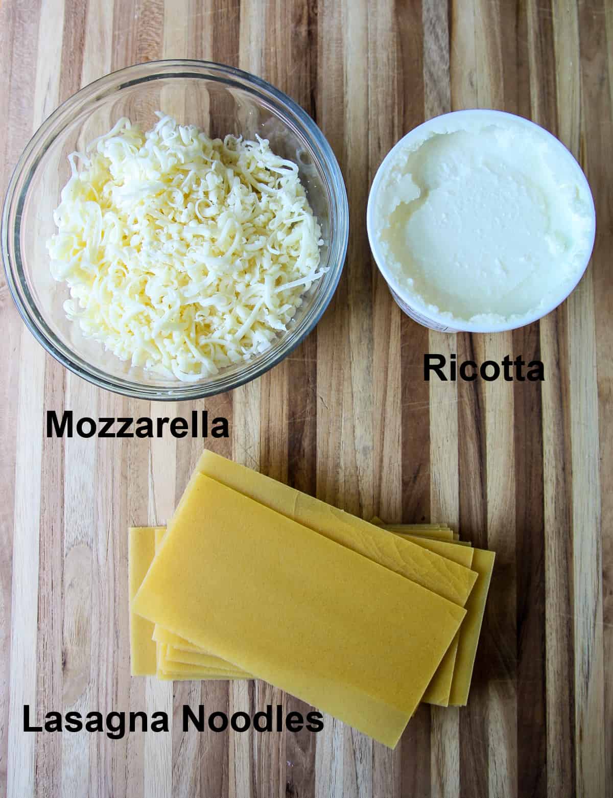 The cheeses and uncooked lasagna noodles for the recipe on a wooden board.