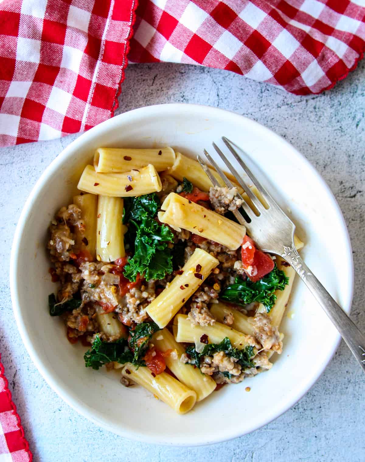 Sausage and kale pasta in a white dish with a silver fork.