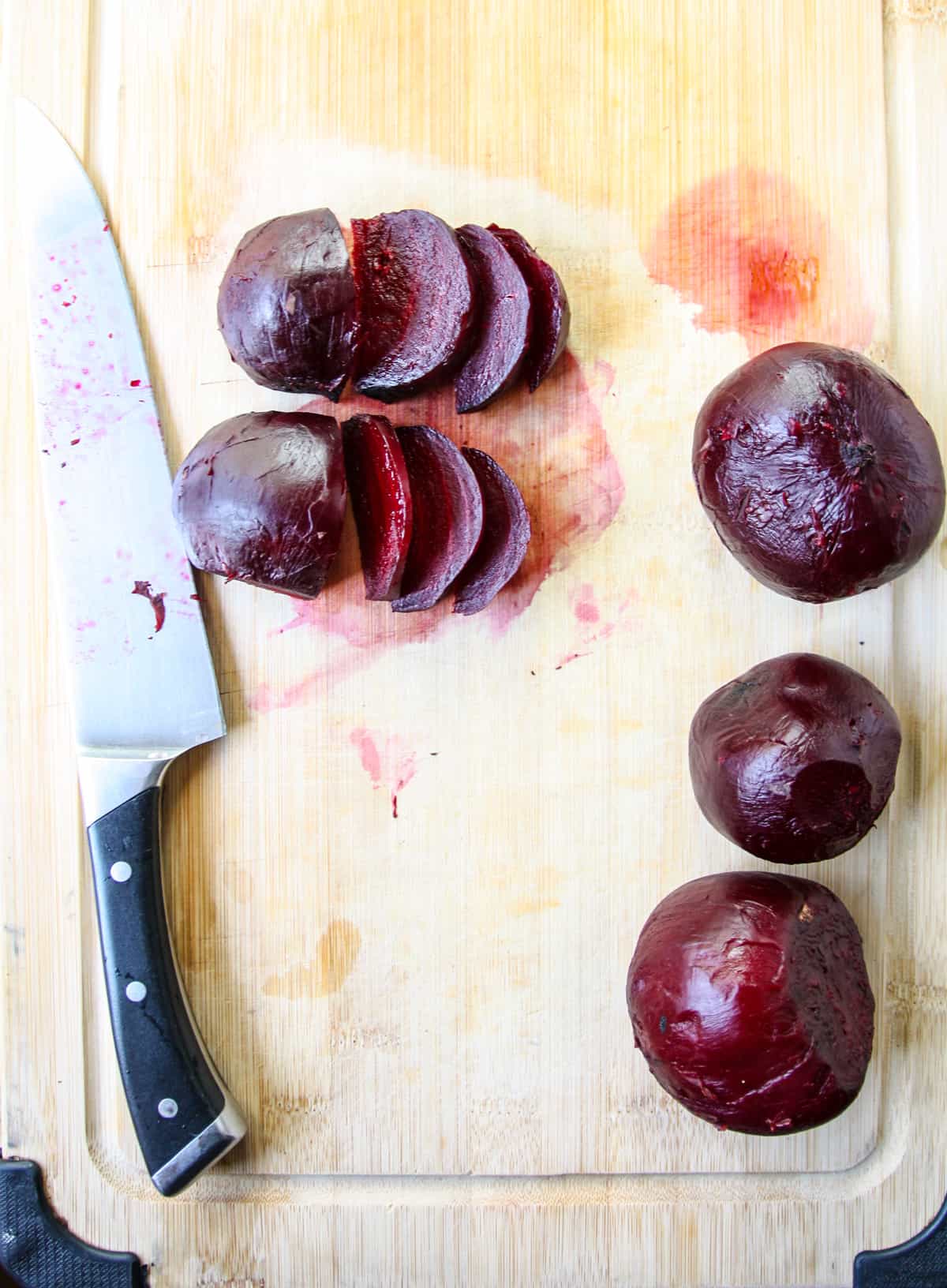Cooked and peeled beets on a cutting board, sliced with a knife.