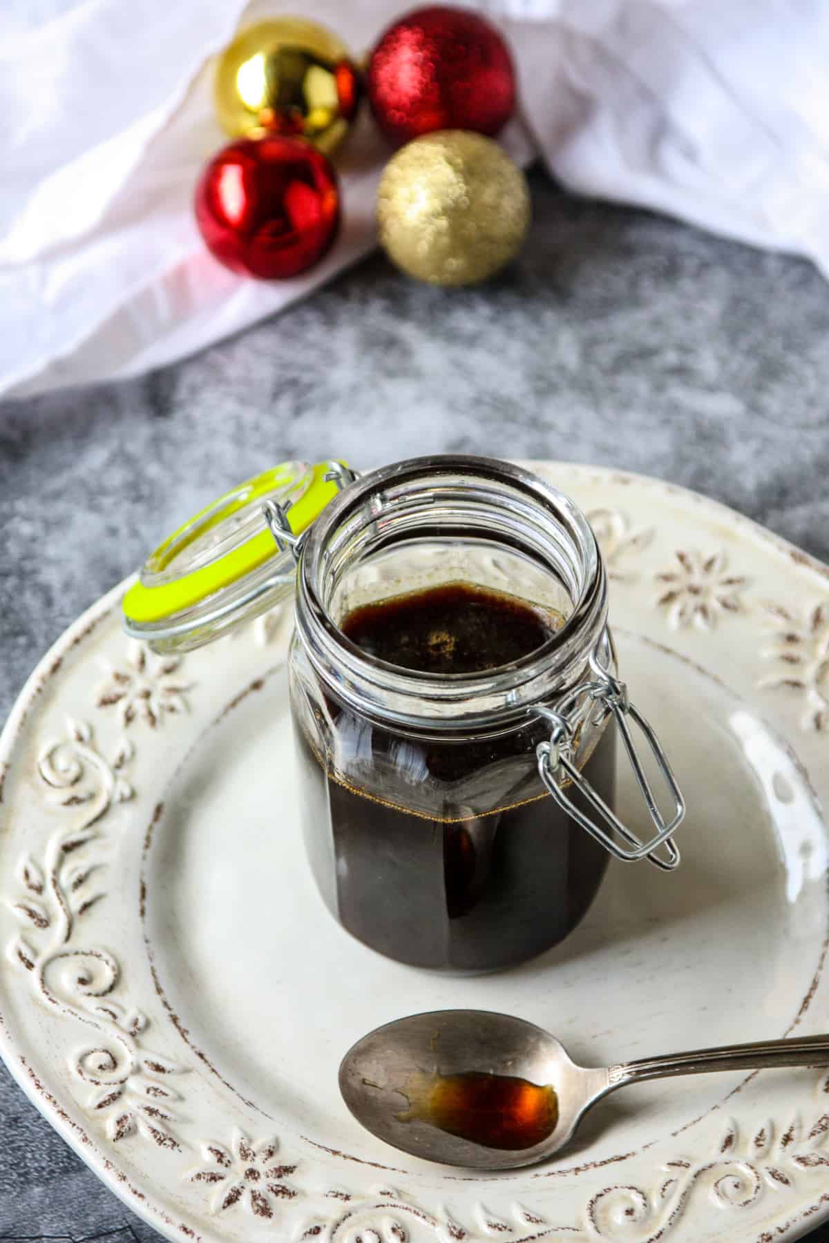 A glass jar filled with gingerbread syrup on a white plate with a silver spoon.