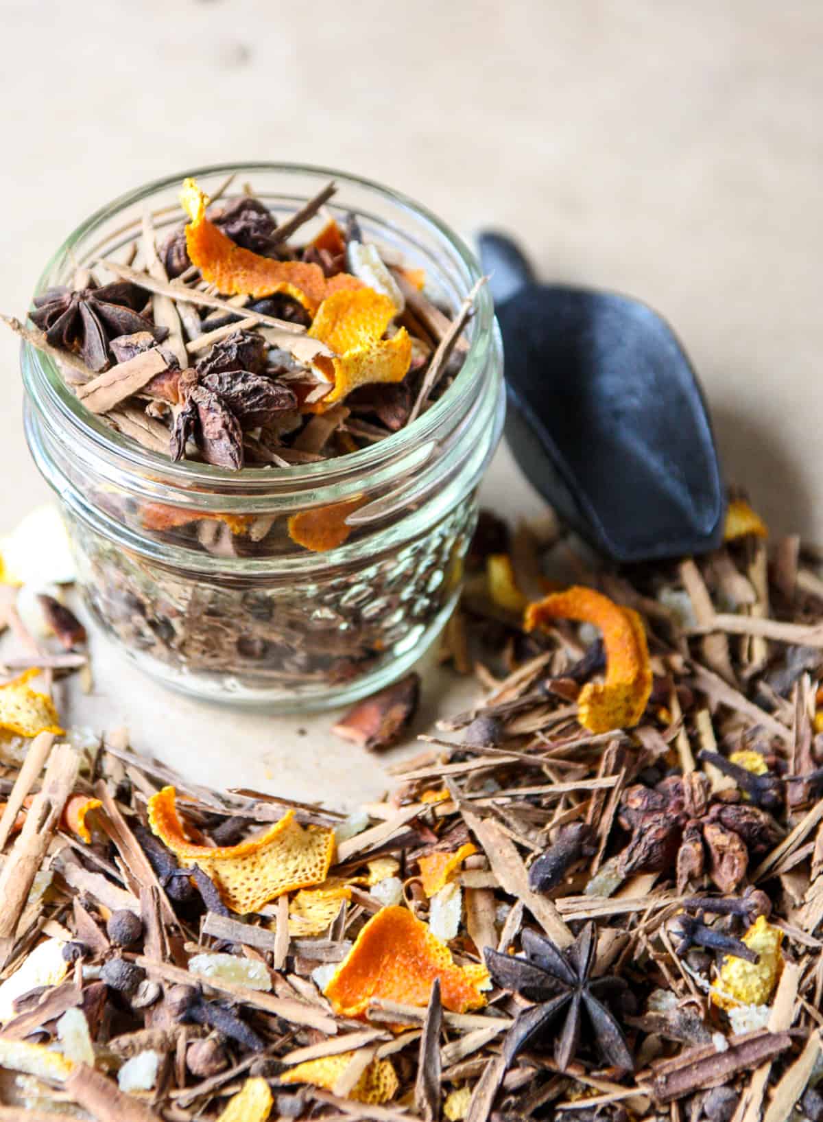 mulling spices spread over a table with a filled glass jar of spice mix.