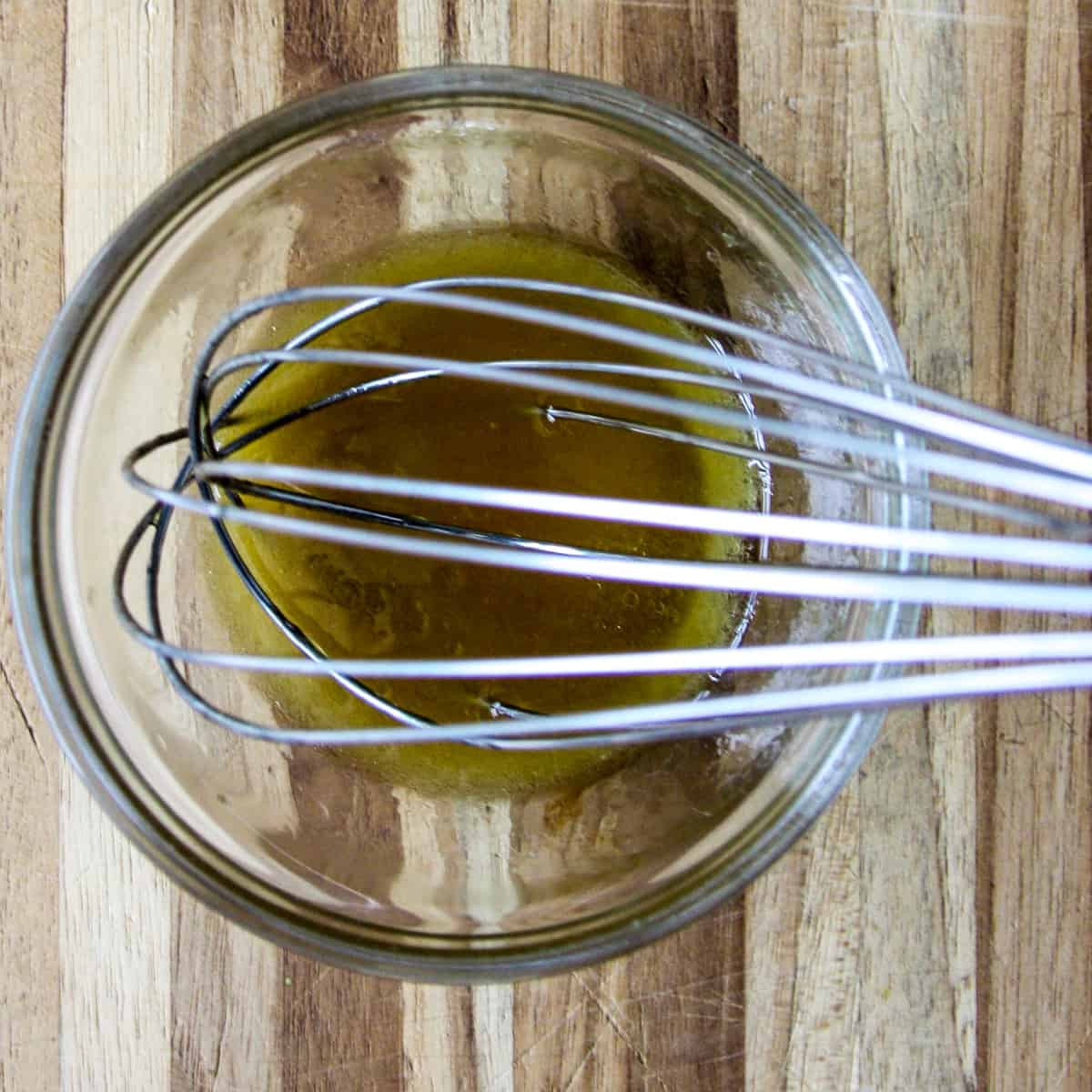 The dressing ingredients being whisked together in a glass bowl.