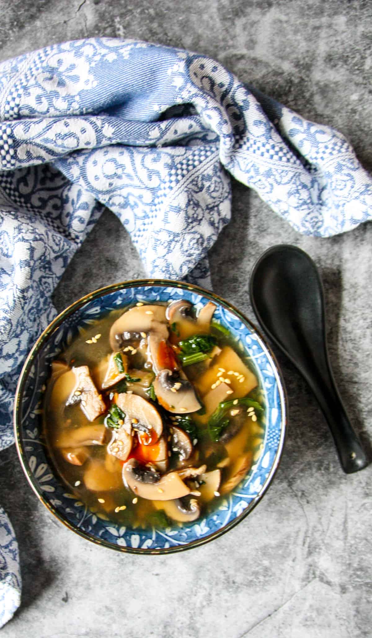 Miso mushroom soup in a bowl, garnished with sesame seeds and droplets of hot sauce.