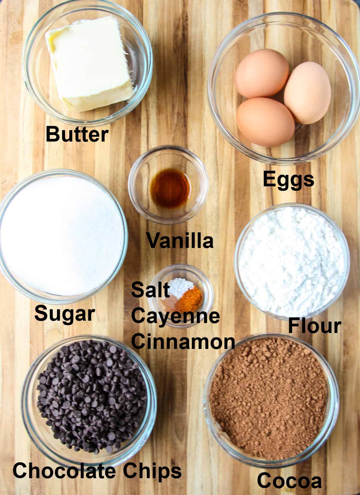All of the recipe ingredients in glass bowls on a wooden board.