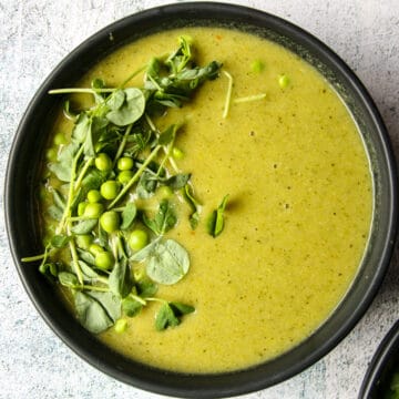 Bright green broccoli and pea soup in a black bowl.