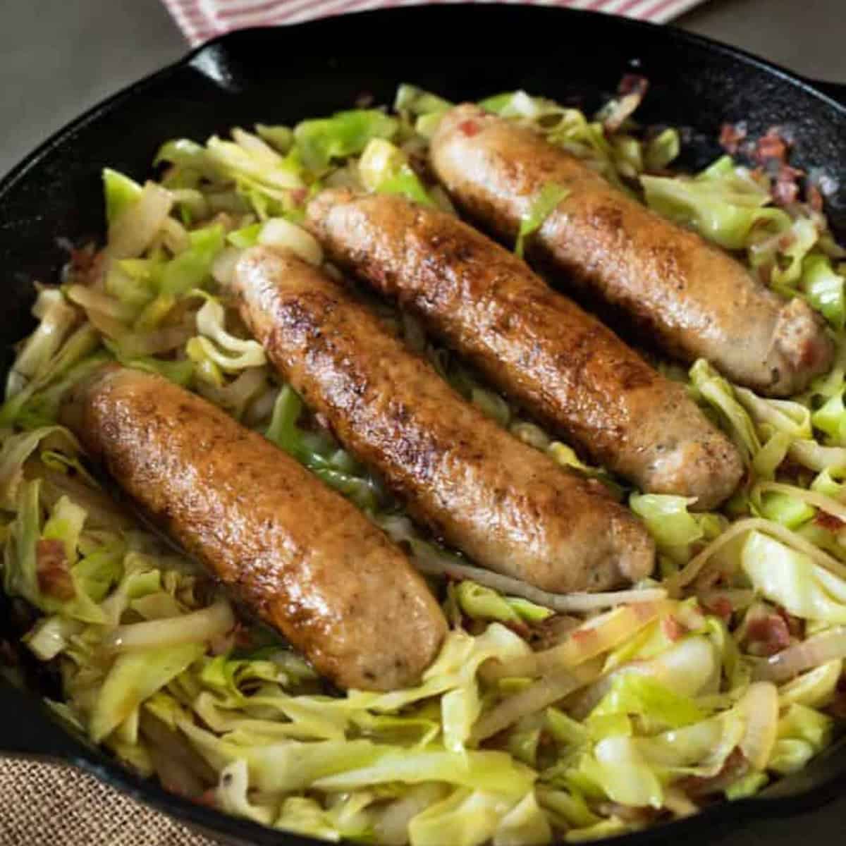 Sausages on a bed of cooked cabbage in a cast iron pan.
