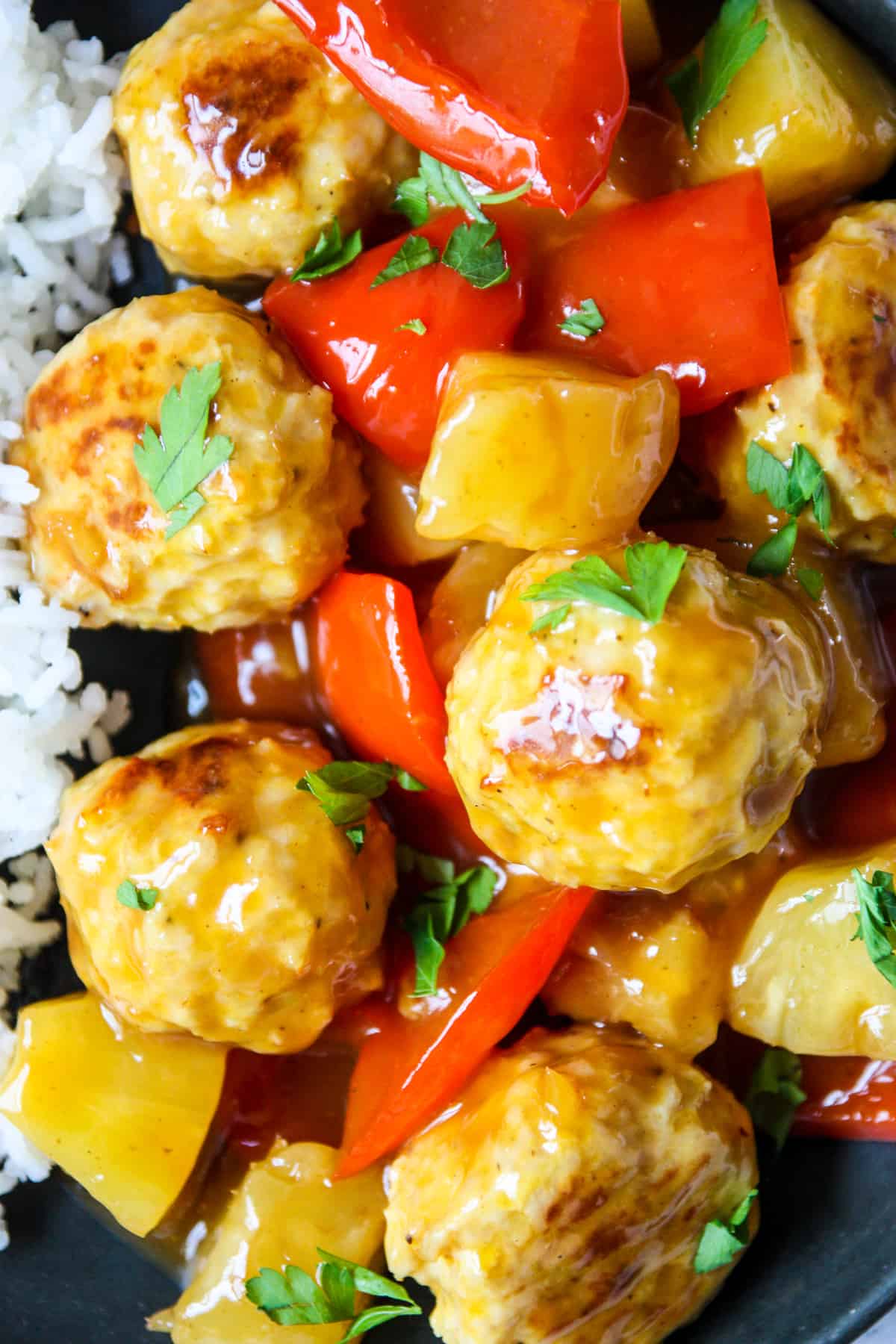 A close shot of sweet and sour meatballs with pineapple and red pepper chunks.