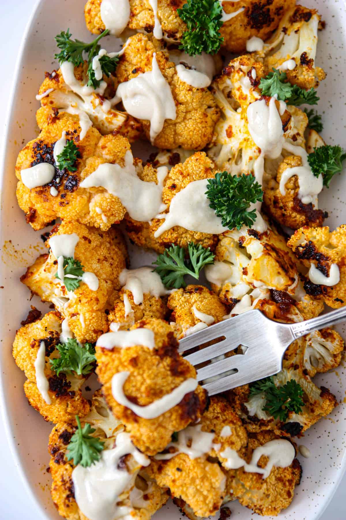 Roasted cauliflower with tahini on a white serving platter with a silver spoon.