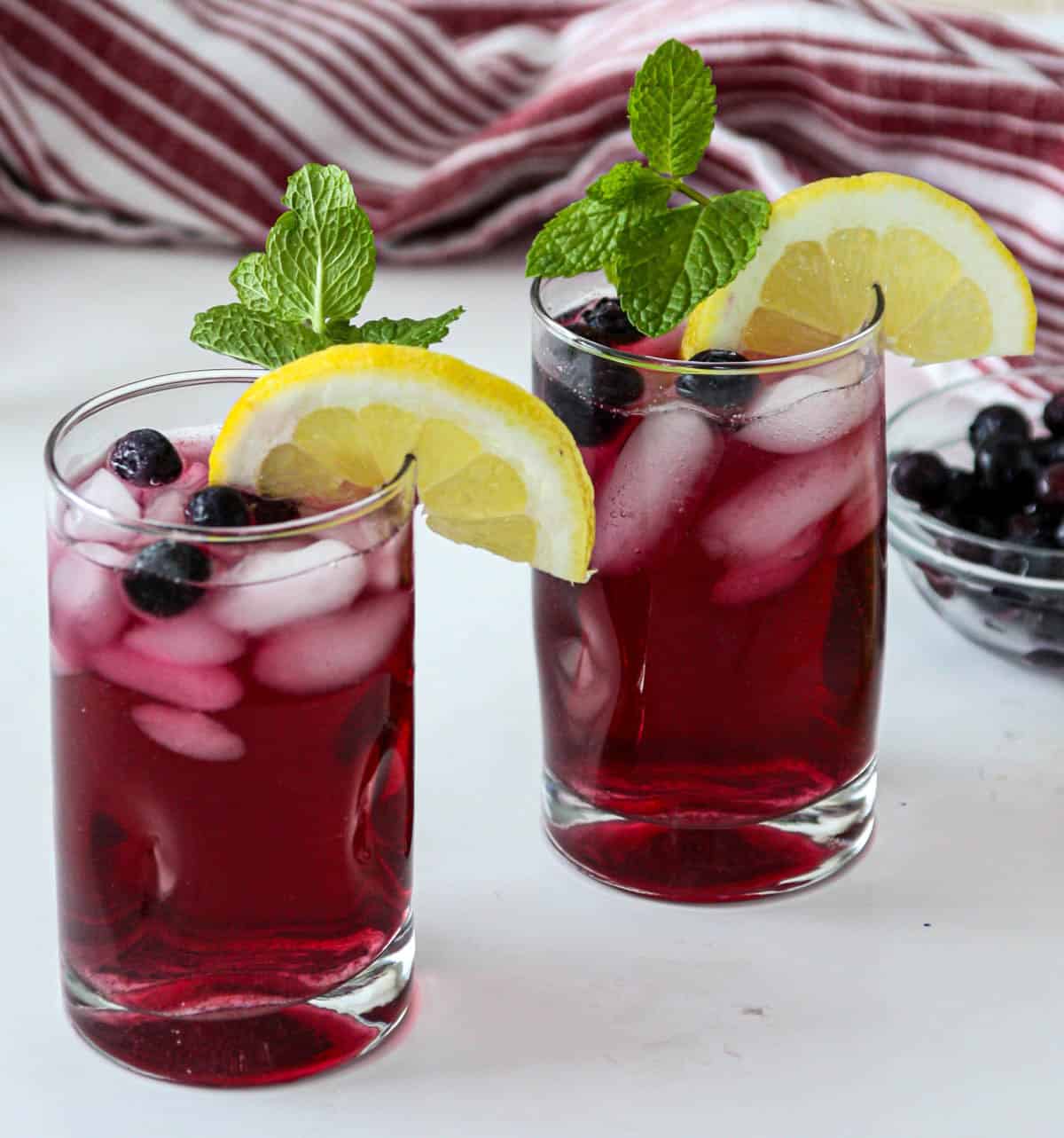 Two glasses of blueberry iced tea, garnished with lemon slices and mint leaves.
