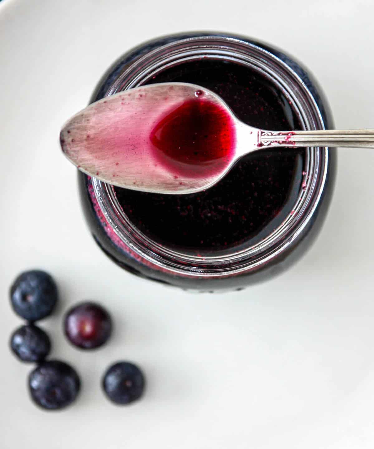A silver spoon in a jar of blueberry simple syrup.