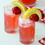 Two glasses of rhubarb lemonade, garnished with lemon slices and strawberries.