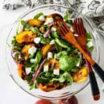 Grilled peach salad in a glass bowl with two wooden forks.