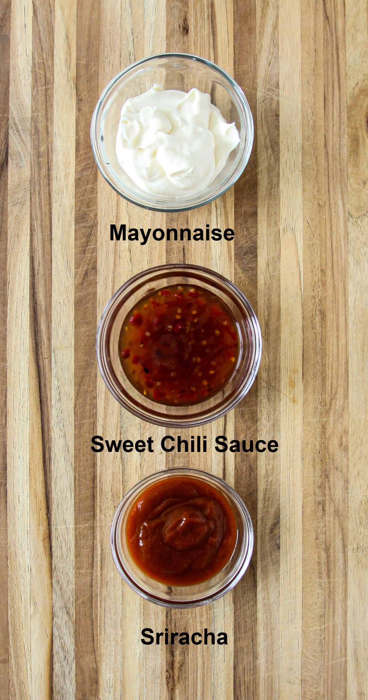 The ingredients for making bang bang sauce, in glass bowls on a wooden board.