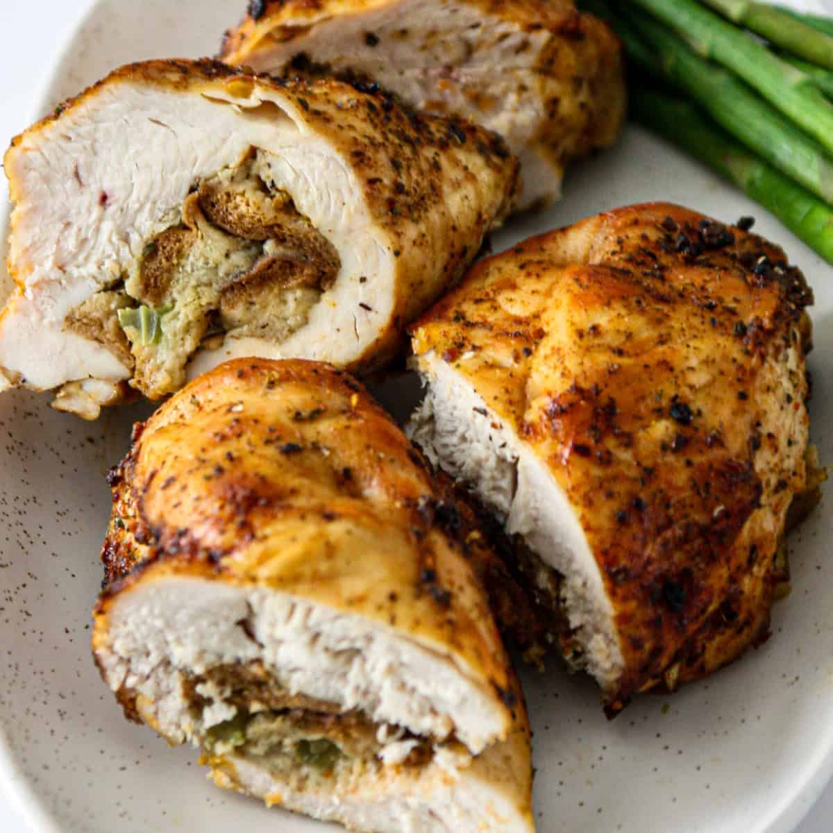Four stuffed chicken breast halves on a white plate.