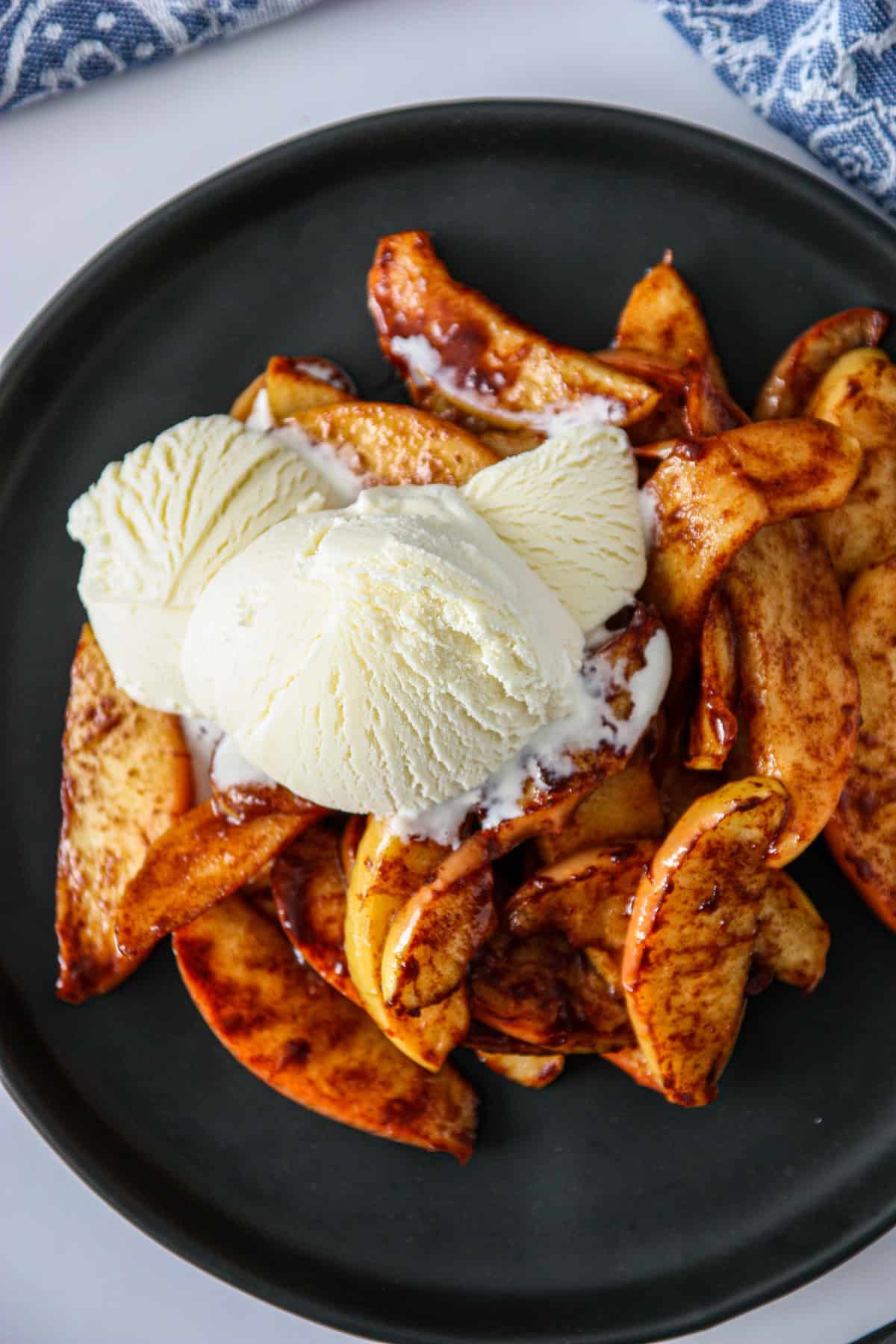 Air fryer apples on a black plate with a scoop of vanilla ice cream.